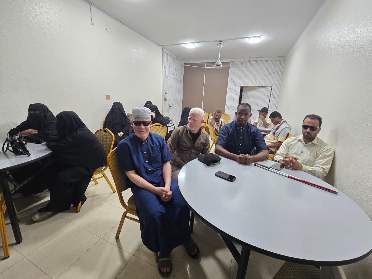 عدد من المشاركين والمشاركات يجلسون في قاعة الدورة، وتظهر عصا بيضاء على الطاولة